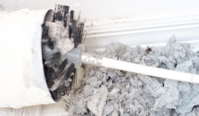 Dryer vent being cleaned, with a large amount of lint and debris being removed by a brush.